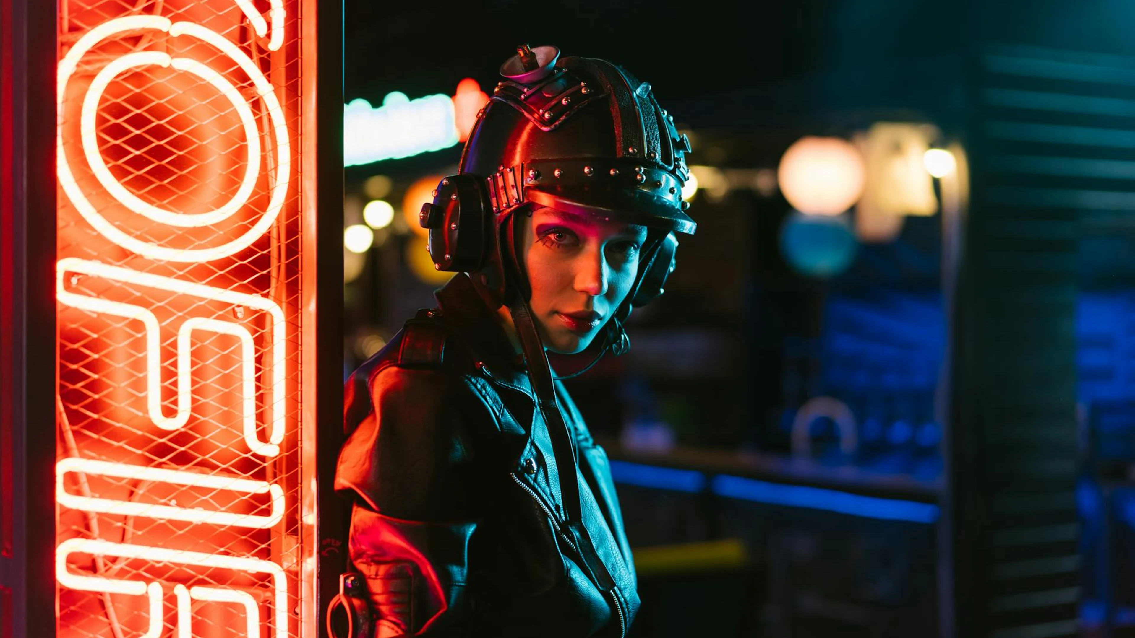 Woman in cyberpunk attire standing by neon sign in an urban setting. - free 4K Ultra HD neon wallpaper for desktop