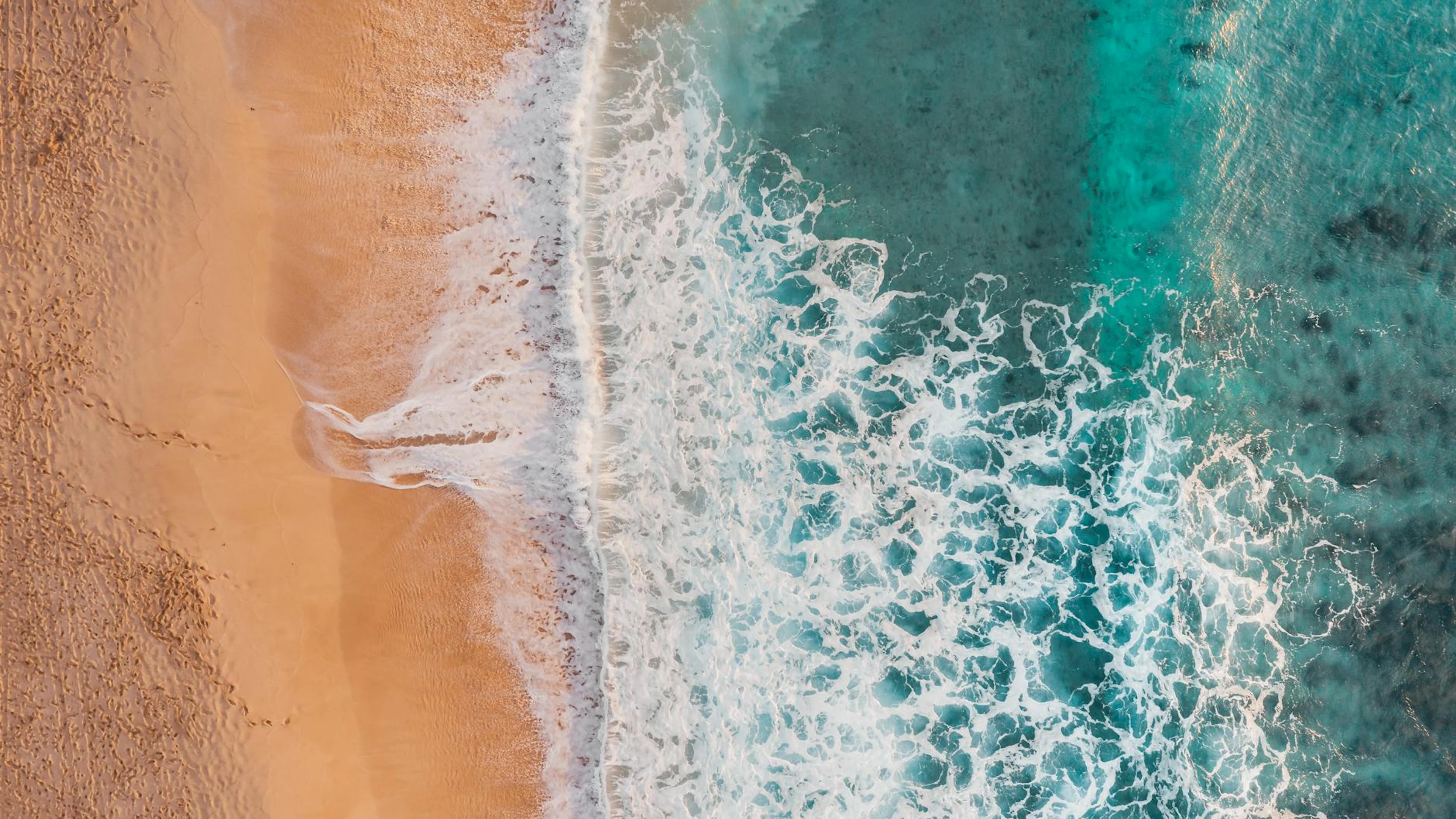 A mesmerizing aerial view of waves crashing onto a sandy tropical beach. - free 4K Ultra HD ocean wallpaper for desktop
