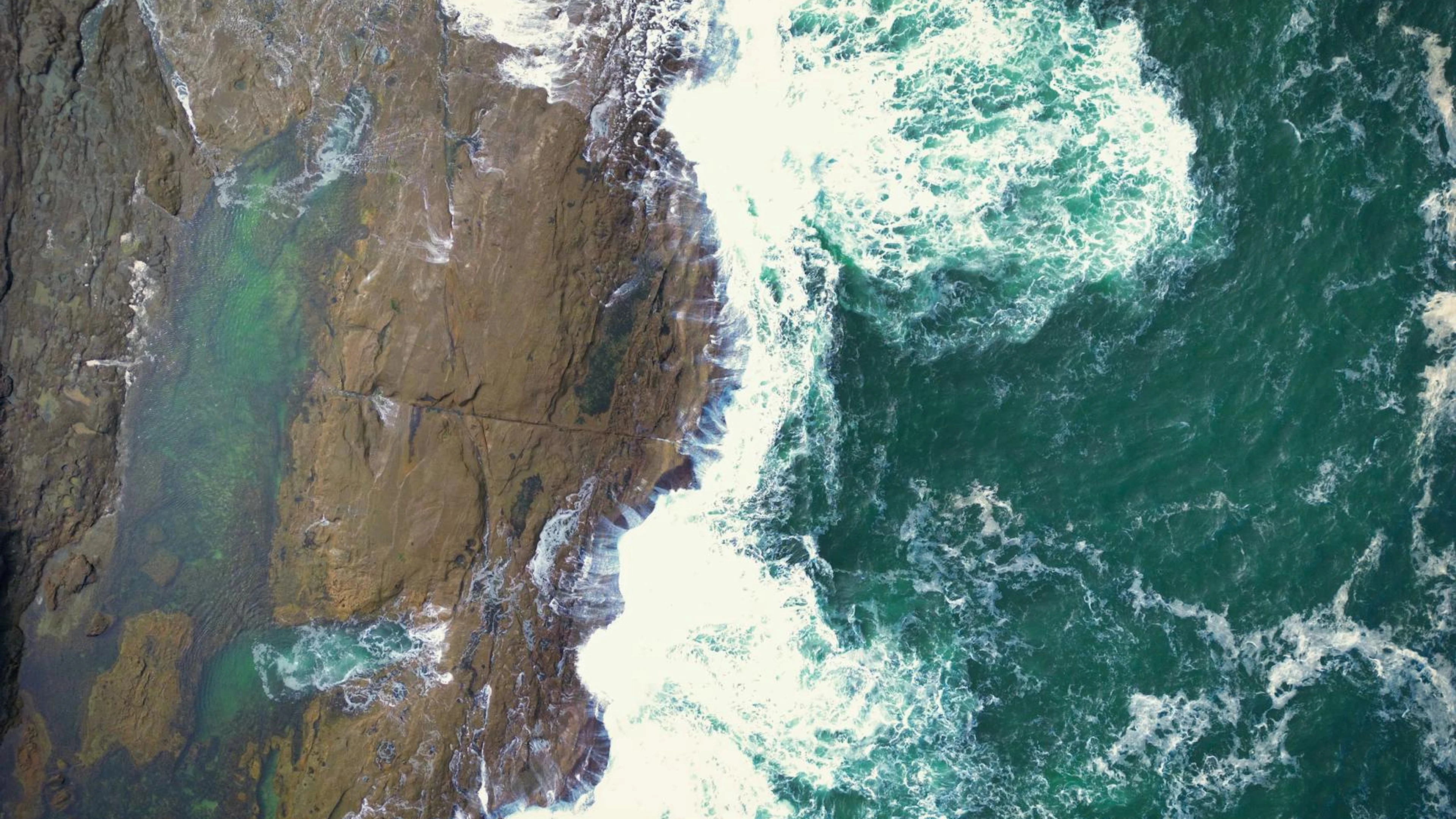A stunning aerial shot capturing waves crashing onto a rocky coastline in Newcas - free 4K Ultra HD ocean wallpaper for desktop