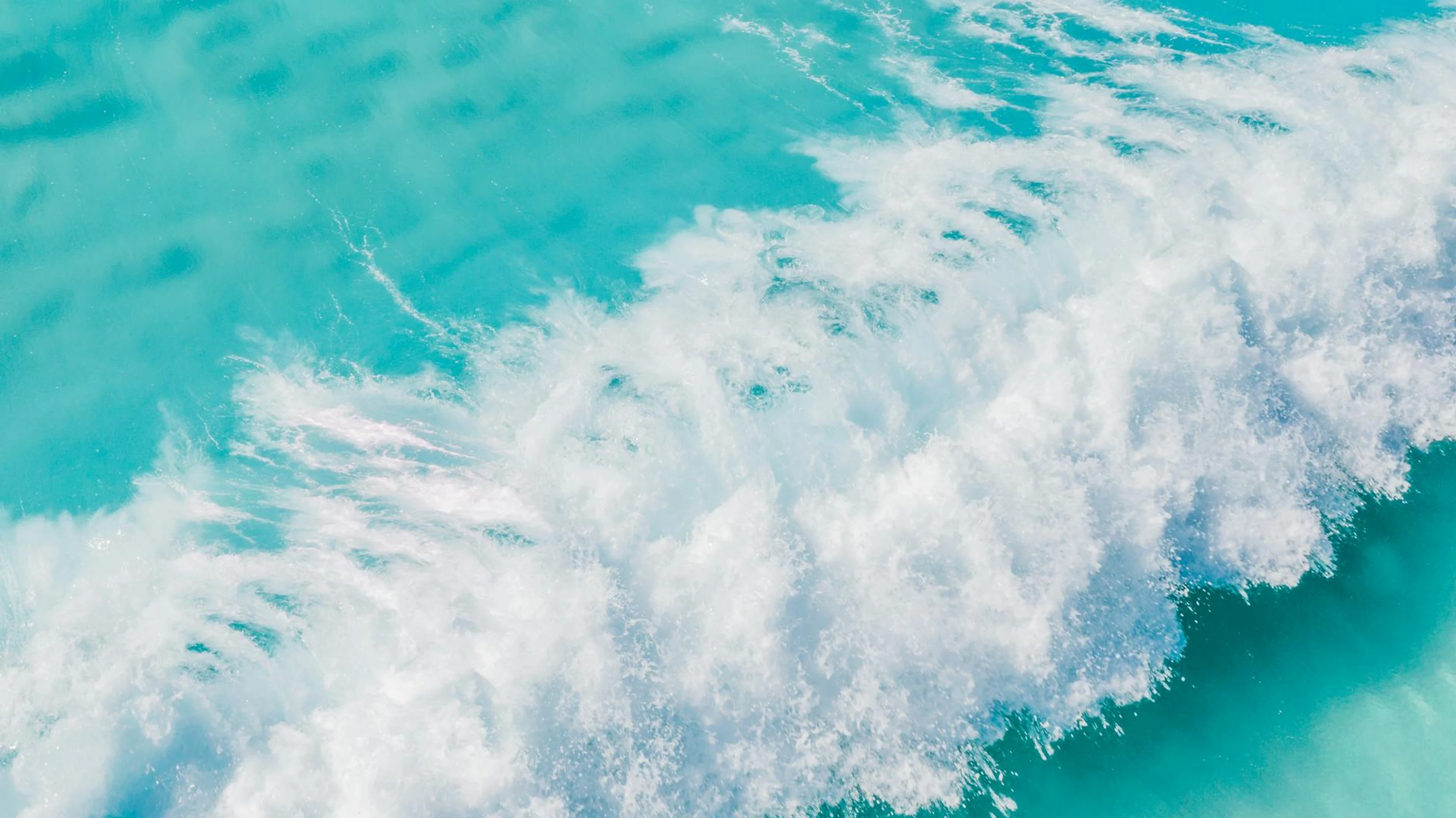 A stunning aerial shot of turquoise waves crashing in the vast ocean, creating a - free 4K Ultra HD ocean wallpaper for desktop