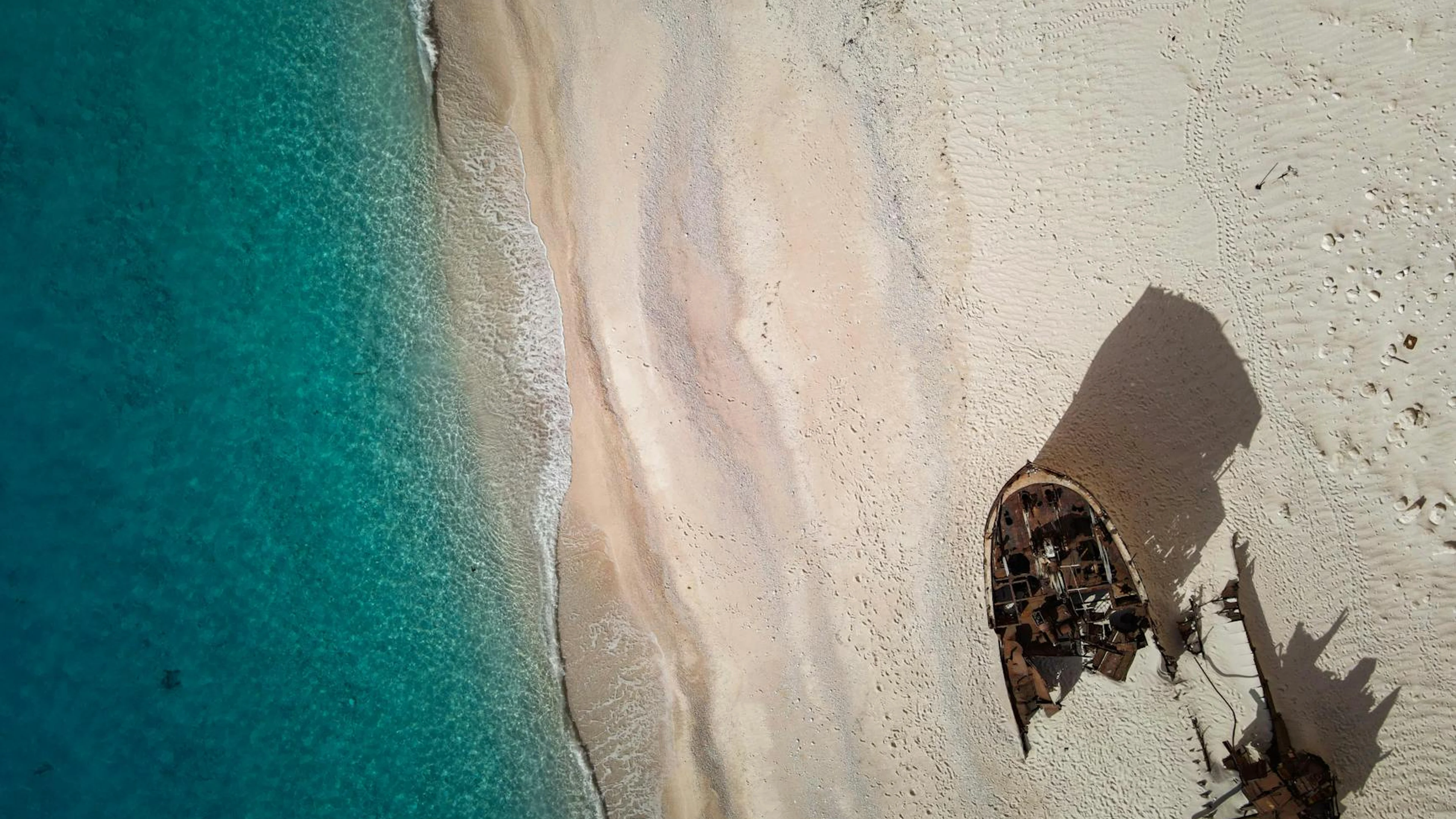 A stunning aerial view of a rusty shipwreck on a remote, sandy beach with turquo - free 4K Ultra HD ocean wallpaper for desktop