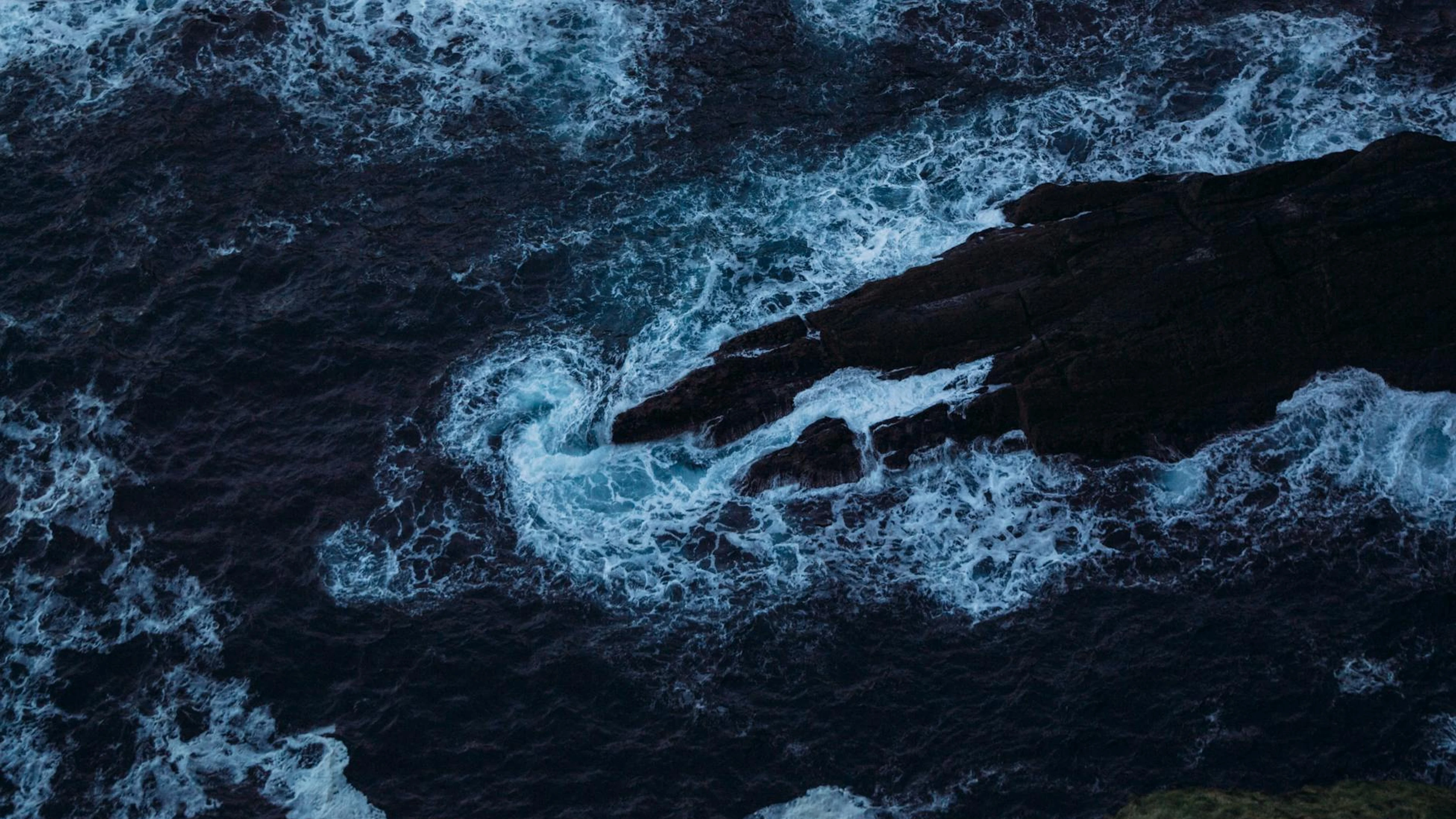 Dramatic aerial capture of ocean waves crashing against rugged rock formations. - free 4K Ultra HD ocean wallpaper for desktop
