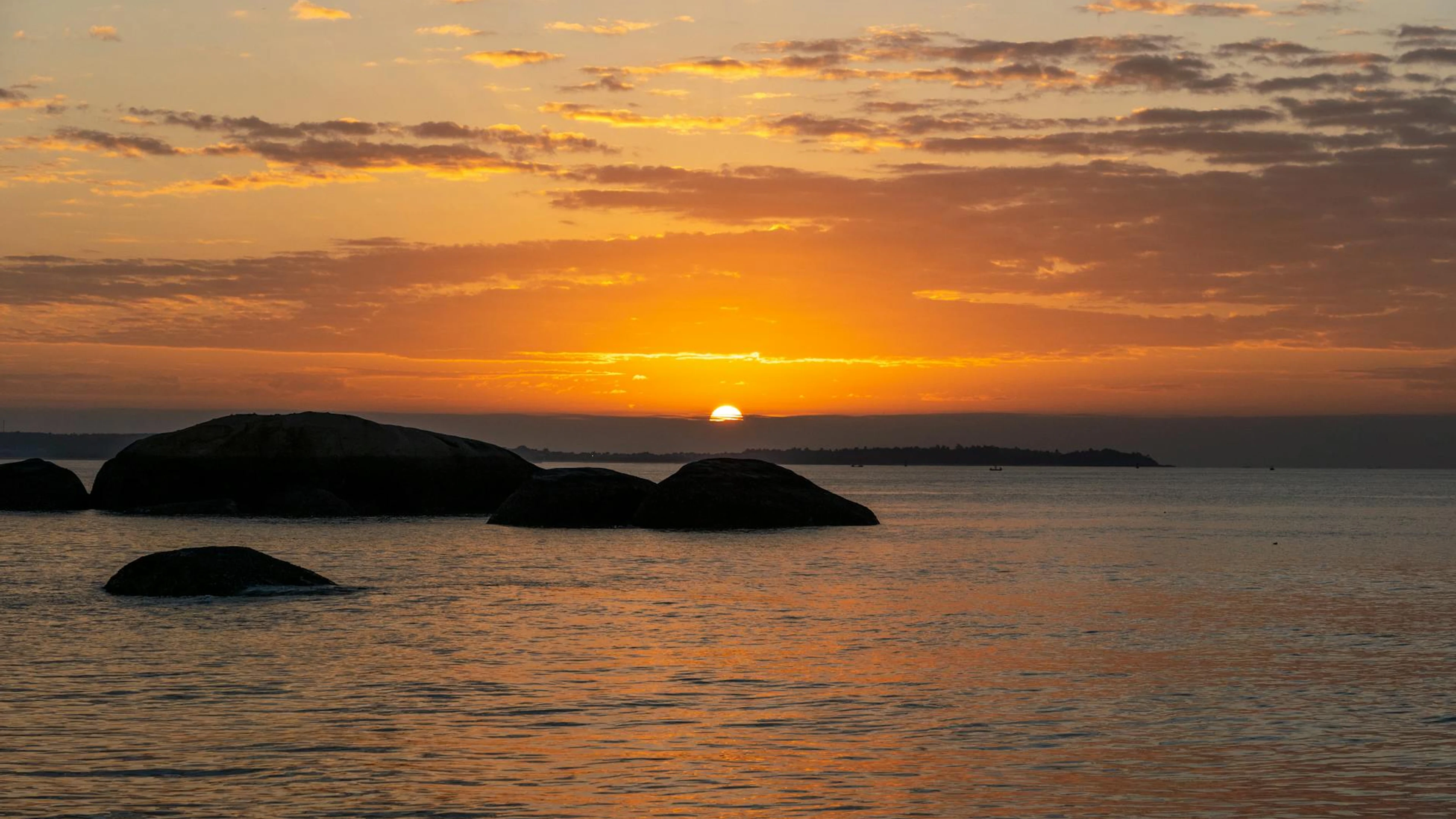 A breathtaking ocean sunset with rocks silhouetted against vibrant orange and ye - free 4K Ultra HD sunset wallpaper for desktop
