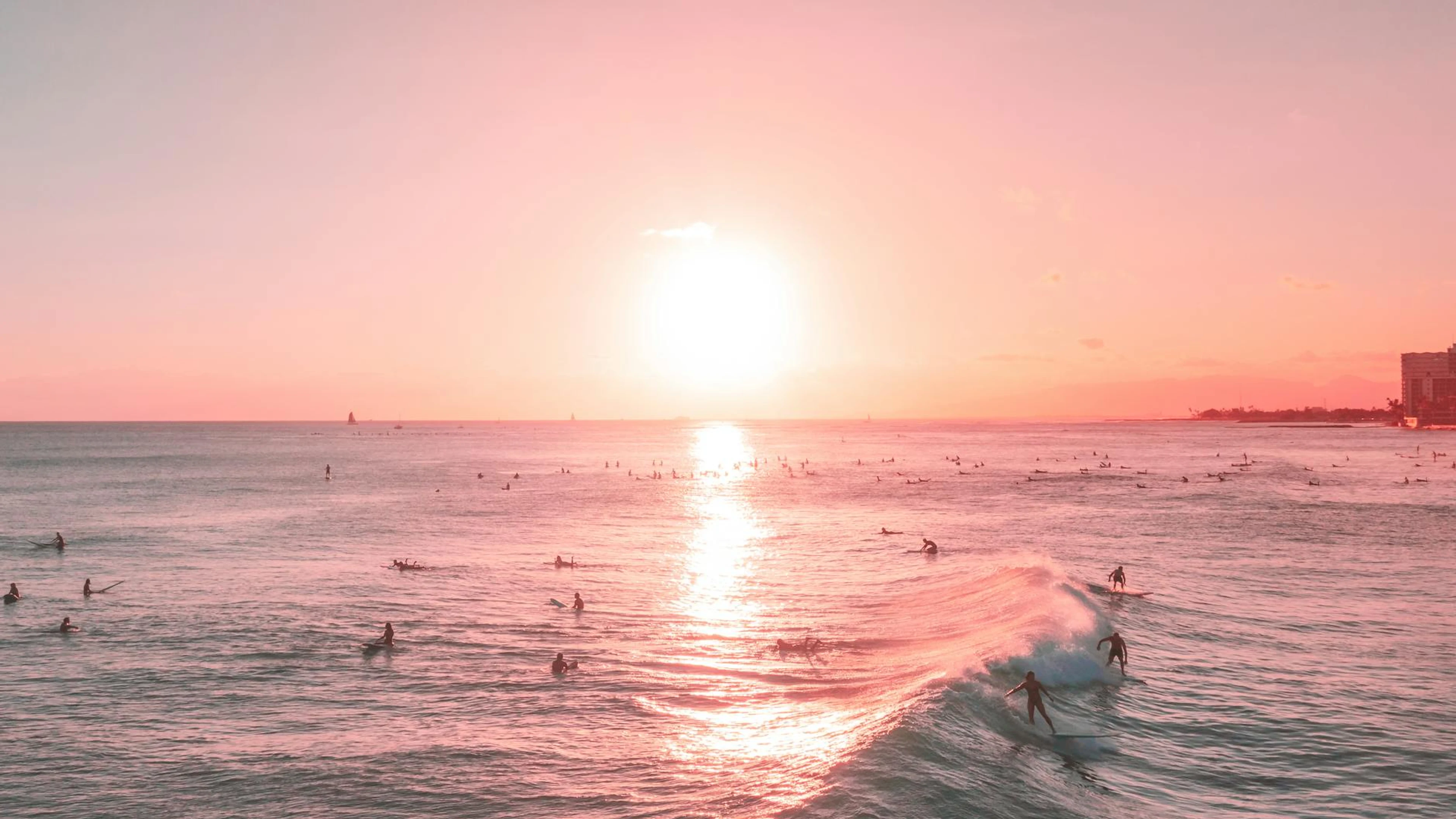 A vibrant sunset scene with surfers riding waves on a summer beach. - free 4K Ultra HD sunset wallpaper for desktop
