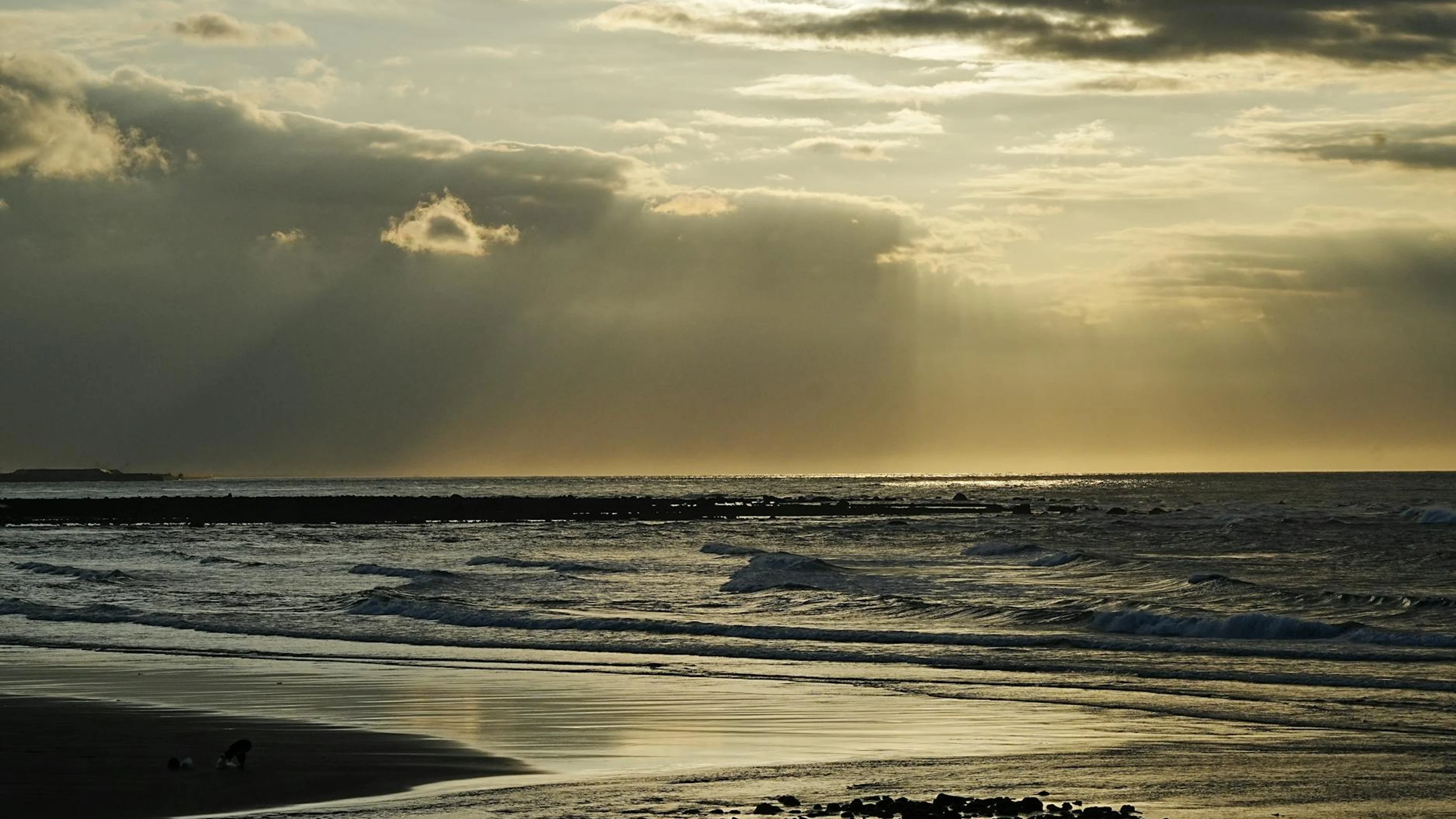 Peaceful coastal sunset with waves and dramatic clouds casting shadows. - free 4K Ultra HD sunset wallpaper for desktop