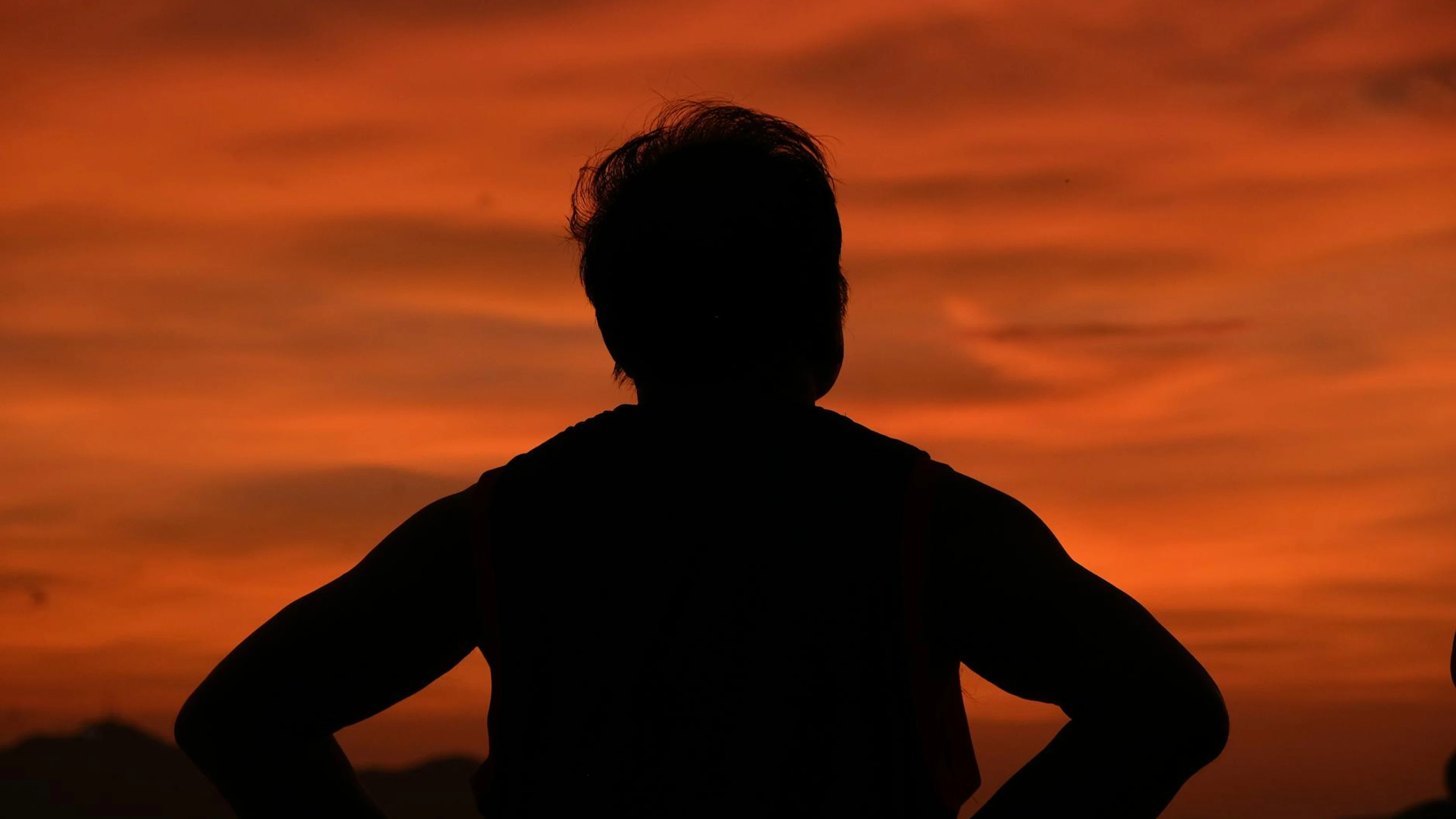 Silhouette of a person standing against a vibrant orange sunset, creating a dram - free 4K Ultra HD sunset wallpaper for desktop