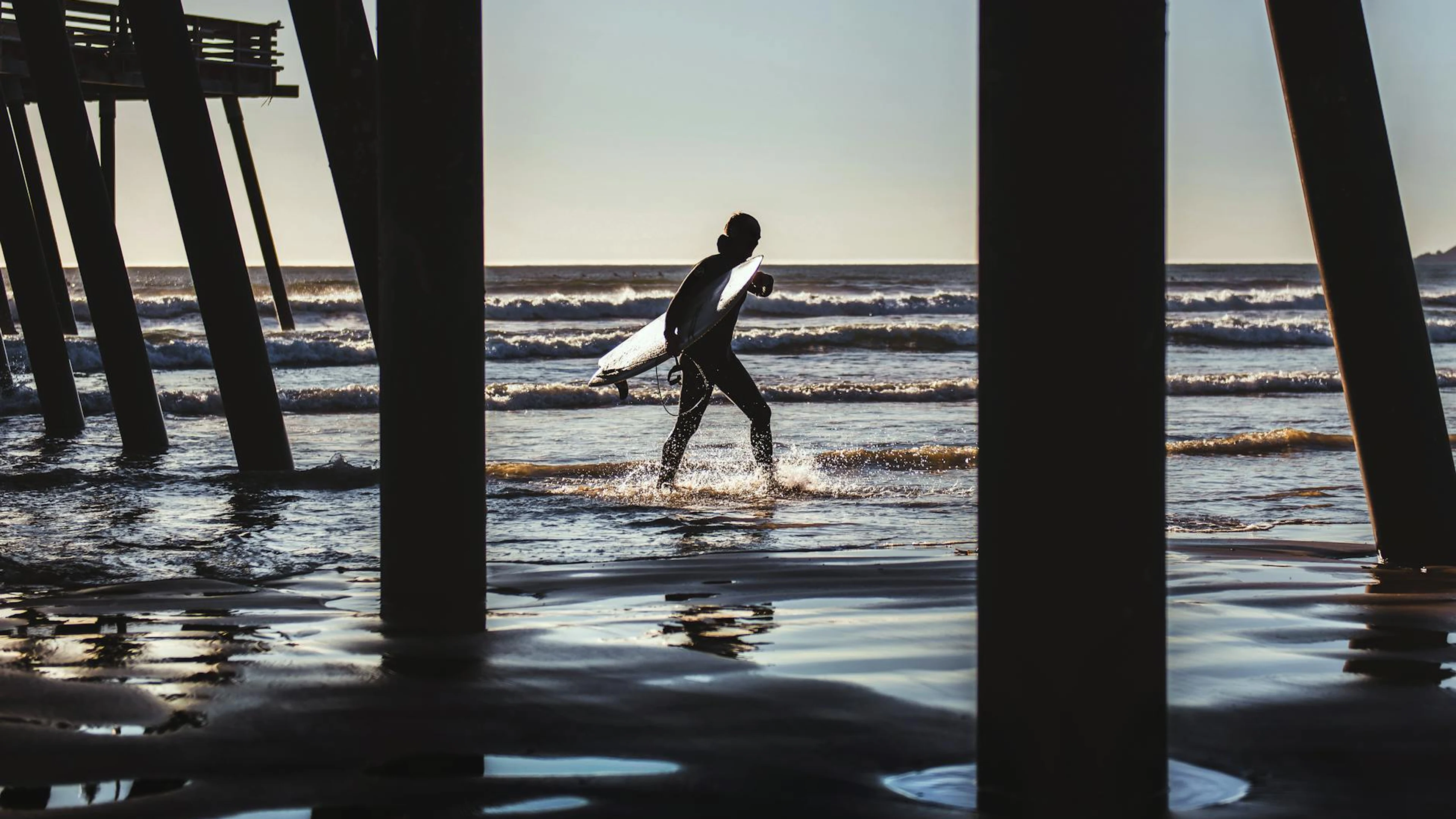 Silhouette of a surfer under Pismo Beach Pier during a stunning California sunse - free 4K Ultra HD sunset wallpaper for desktop