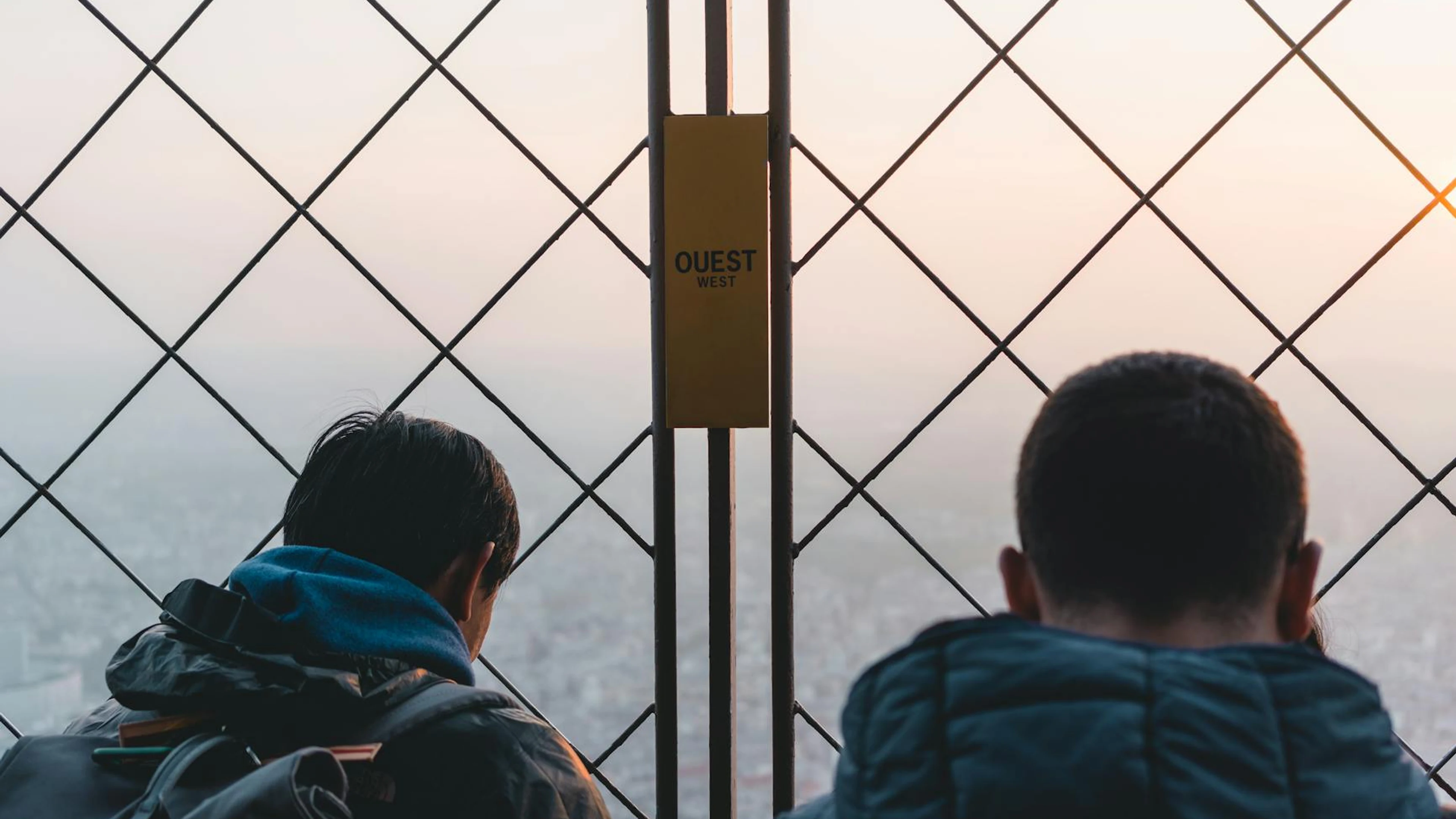 Two men overlooking a city skyline through a fence during sunset, facing westwar - free 4K Ultra HD sunset wallpaper for desktop